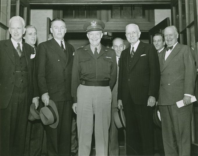 General of the Army Eisenhower pauses for a minute as he emerges from Kirby Hall, after his meeting with the college's Board of Trustees. Left to right are the Hon. William H. Kirpatrick; Mr. F.J. Waltzinger, Dr. Hutchinson; General of the Army Eisenhower, Mr. T. F. Soles, Mr. Thos. J. Watson, Mr. Thomas W. Pomeroy and Mr. Francis G McKelvy.