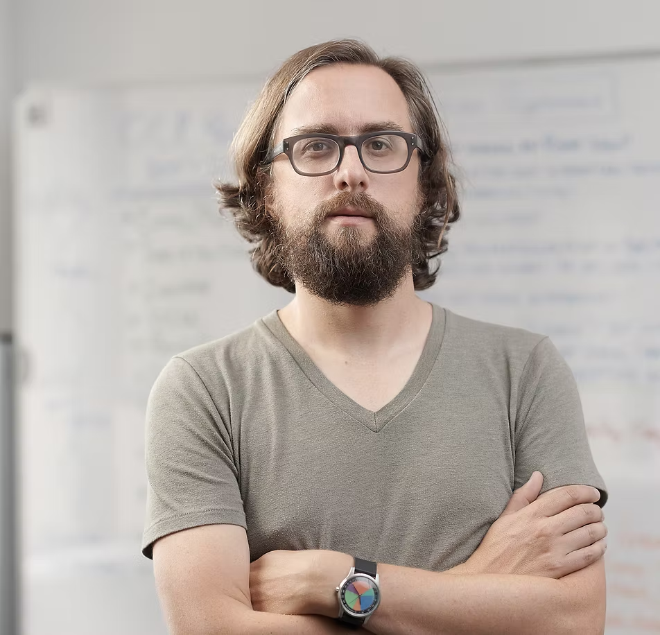 Headshot of Jer Thorpe, wearing glasses and standing in front of a white board that has been blurred int he background.